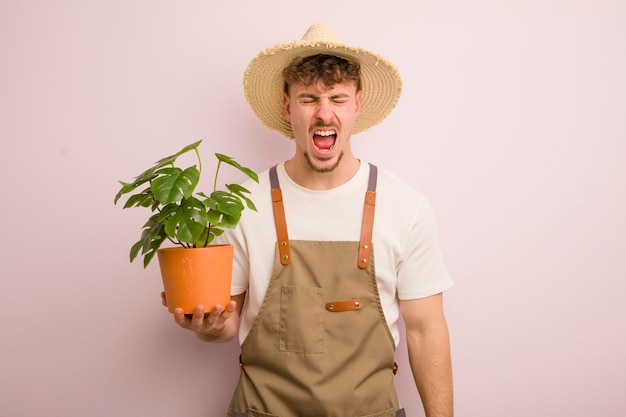 Joven genial gritando agresivamente con aspecto de jardinero y planta muy enojados