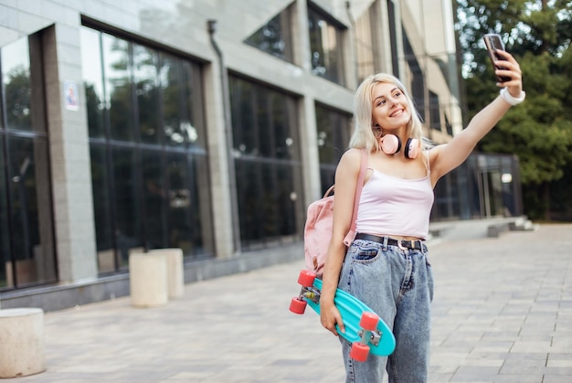 Una joven genial con patineta se hace una selfie en el teléfono en la ciudad.