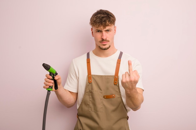 Joven genial que se siente enojado, molesto, rebelde y agresivo, jardinero y concepto de manguera