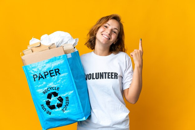 Joven georgiana sosteniendo una bolsa de reciclaje llena de papel para reciclar apuntando hacia una gran idea