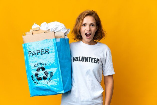 Joven georgiana sosteniendo una bolsa de reciclaje llena de papel para reciclar con expresión facial sorpresa