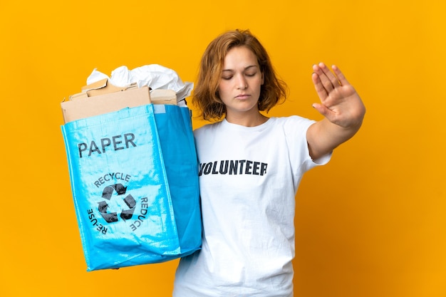 Joven georgiana sosteniendo una bolsa de reciclaje llena de papel para reciclar haciendo gesto de parada y decepcionado