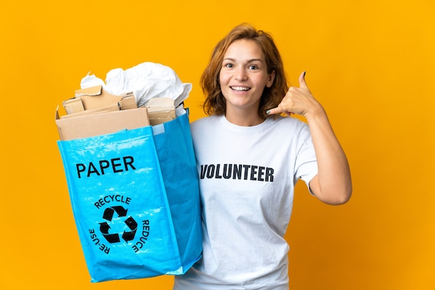 Joven georgiana sosteniendo una bolsa de reciclaje llena de papel para reciclar haciendo gesto de teléfono. Llámame señal