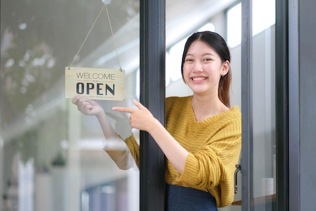 Joven gerente de Asia que cambia un letrero de cerrado a abierto en el café de la puerta mirando afuera esperando a los clientes después del cierre Propietario de pequeñas empresas de alimentos y bebidas reabre de nuevo el concepto