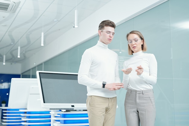 Foto joven gerente de oficina elegante en gafas inteligentes haciendo la presentación de la nueva tableta transparente ultramoderna al cliente y mostrando cómo usarla