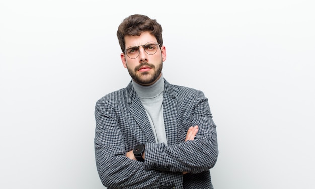 El joven gerente se siente disgustado y decepcionado, se ve serio, molesto y enojado con los brazos cruzados contra la pared blanca