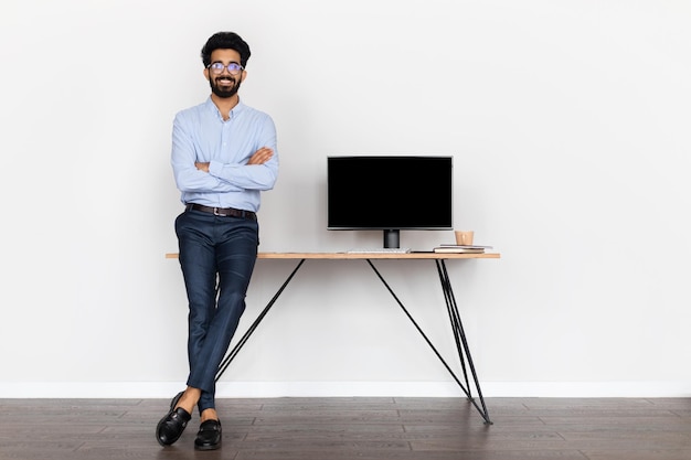 Joven gerente de ti del este junto al escritorio con computadora