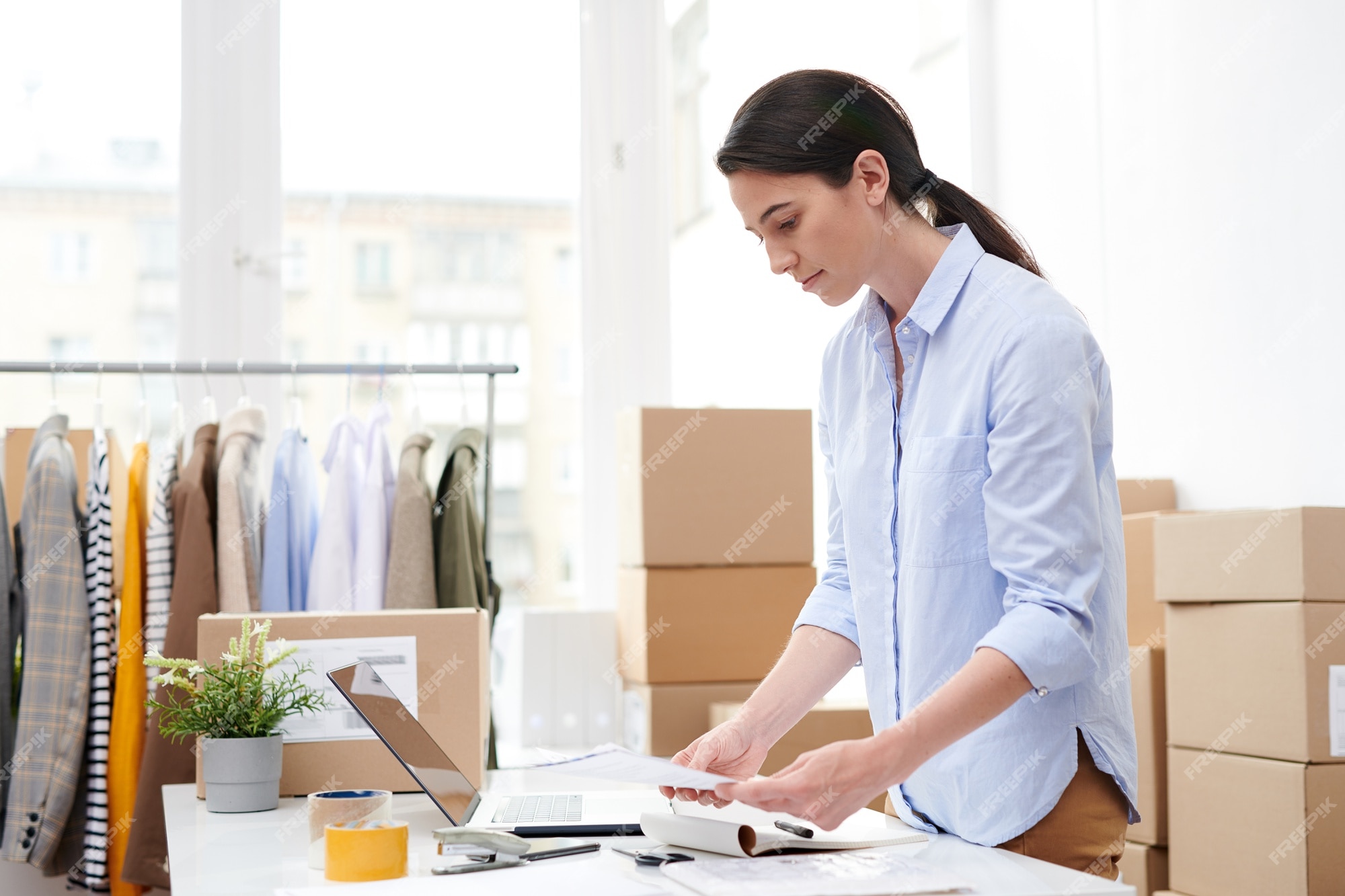 Joven gerente de tienda online de ropa casual mirando folletos para antes de empaquetar sus en cajas |