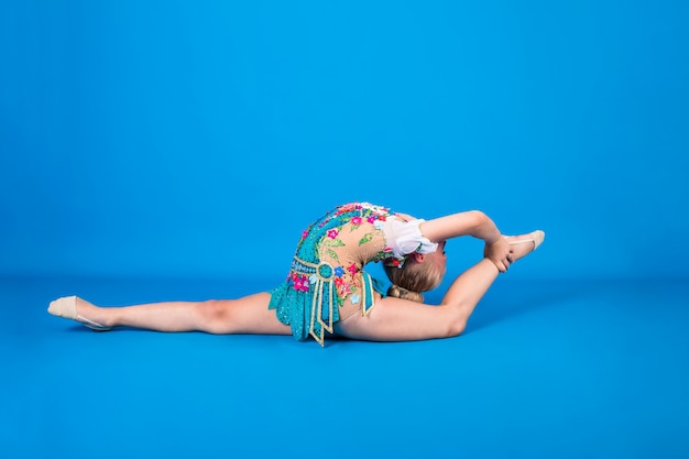 Una joven gimnasta realiza un ejercicio con una desviación en la espalda sobre una pared azul aislada