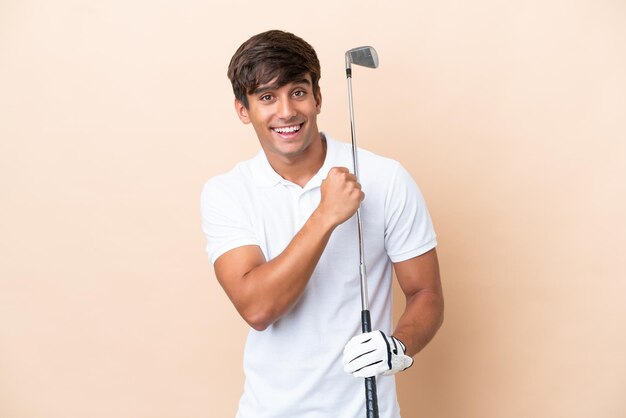 Joven golfista hombre aislado sobre fondo ocre celebrando una victoria