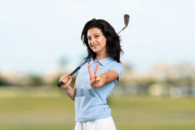 Joven golfista mujer sonriendo y mostrando el signo de la victoria al aire libre