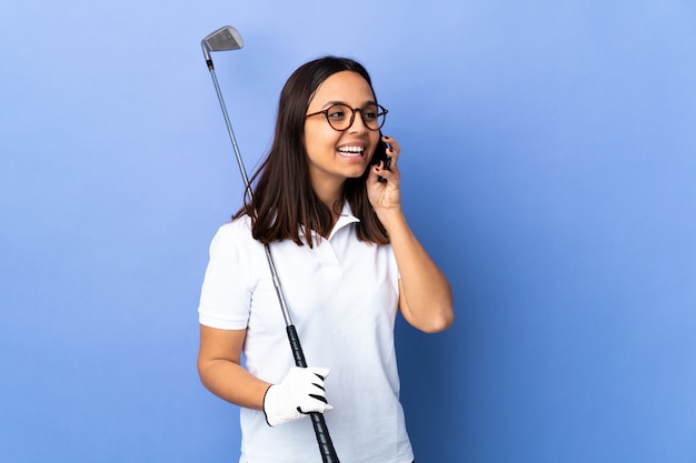 Joven golfista sobre pared colorida manteniendo una conversación con el teléfono móvil