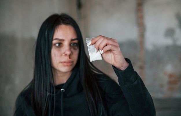 Joven golpeada sosteniendo un paquete con drogas blancas en la mano