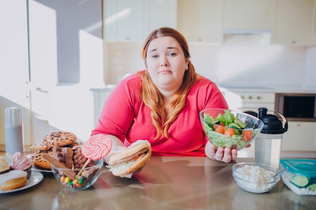 Joven gorda en la cocina sentado y comiendo comida