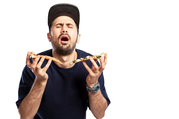 Un joven con gorra come pizza con placer. Aislado sobre fondo blanco. Espacio para texto.