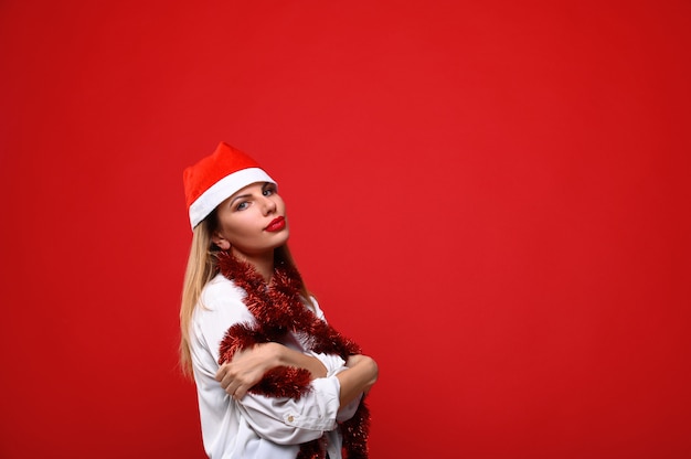 La joven con gorro de Papá Noel con una guirnalda de árbol de Navidad alrededor de su cuello. El concepto de Navidad.