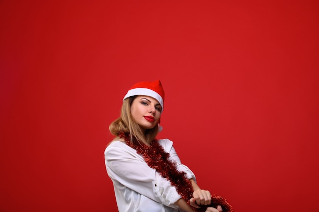 La joven con gorro de Papá Noel con una guirnalda de árbol de Navidad alrededor de su cuello.