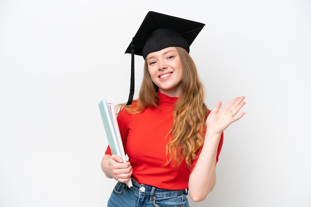 Joven graduada universitaria aislada de fondo blanco saludando con la mano con expresión feliz