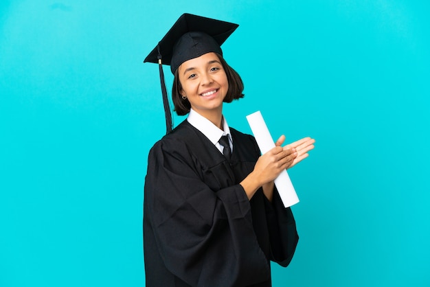 Joven graduada universitaria sobre fondo azul aislado aplaudiendo