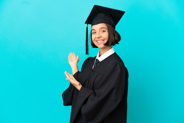 Joven graduada universitaria sobre fondo azul aislado extendiendo las manos hacia el lado para invitar a venir