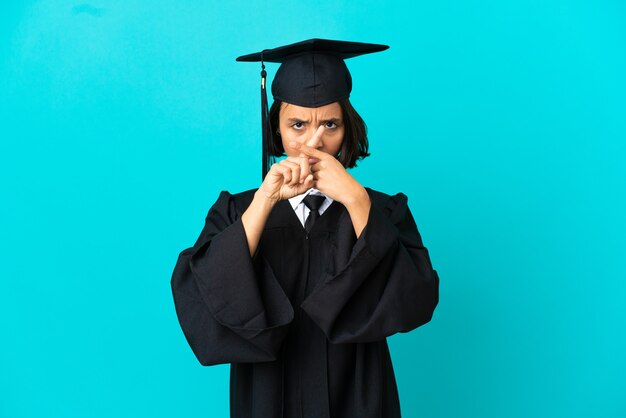 Joven graduada universitaria sobre fondo azul aislado haciendo gesto de parada con la mano para detener un acto