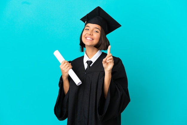 Joven graduada universitaria sobre fondo azul aislado mostrando y levantando un dedo