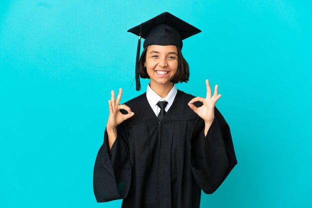 Joven graduada universitaria sobre fondo azul aislado mostrando signo de ok con las dos manos