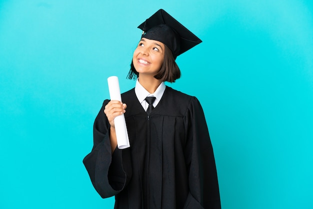 Joven graduada universitaria sobre fondo azul aislado pensando en una idea mientras mira hacia arriba