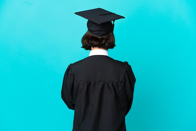 Joven graduada universitaria sobre fondo azul aislado en posición trasera