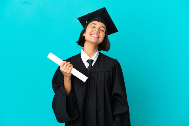 Joven graduada universitaria sobre fondo azul aislado riendo