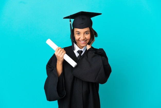 Joven graduada universitaria sobre pared azul aislada riendo