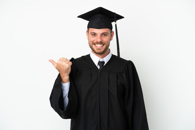 Joven graduado brasileño universitario aislado sobre fondo blanco apuntando hacia el lado para presentar un producto