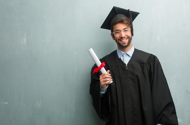 Joven graduado contra una pared de grunge con un espacio de copia alegre y con una gran sonrisa