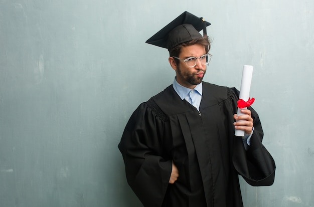 Joven graduado contra una pared de grunge con un espacio de copia muy enojado y molesto