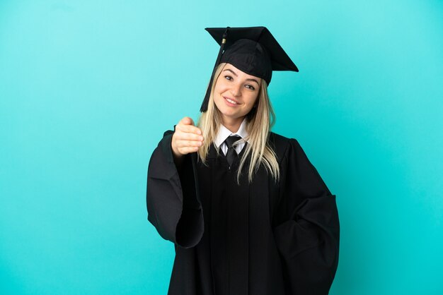 Joven graduado de la universidad sobre fondo azul aislado un apretón de manos para cerrar un buen trato