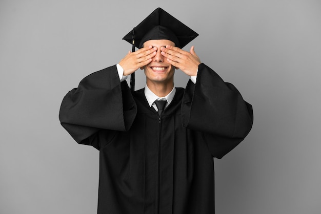 Joven graduado universitario argentino aislado de fondo gris cubriendo los ojos con las manos