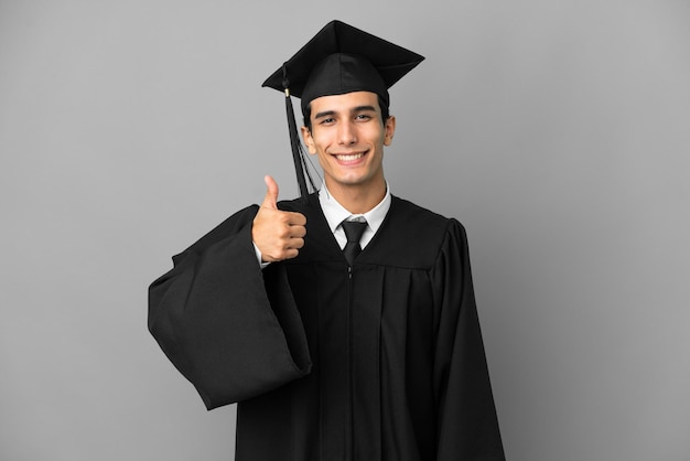 Joven graduado universitario argentino aislado de fondo gris dando un gesto de aprobación