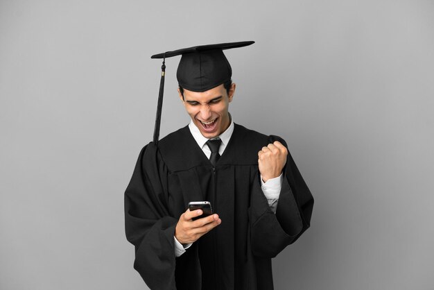 Joven graduado universitario argentino aislado de fondo gris sorprendido y enviando un mensaje