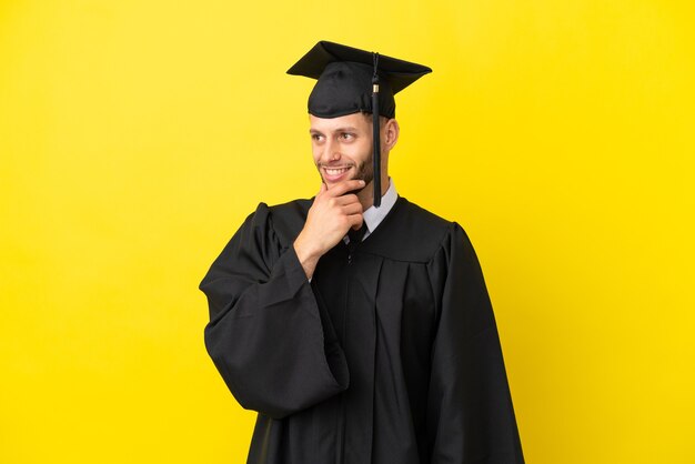 Joven graduado universitario hombre caucásico aislado sobre fondo amarillo mirando hacia el lado