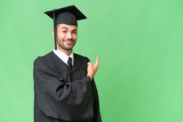 Joven graduado universitario hombre sobre fondo aislado apuntando hacia atrás