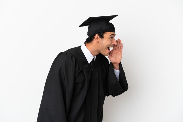 Joven graduado universitario sobre fondo blanco aislado gritando con la boca abierta hacia el lateral