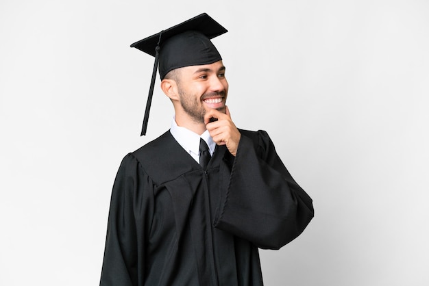 Joven graduado universitario sobre fondo blanco aislado mirando hacia un lado