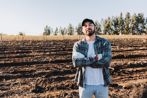 Joven granjero latino con los brazos cruzados en medio de las tierras de cultivo