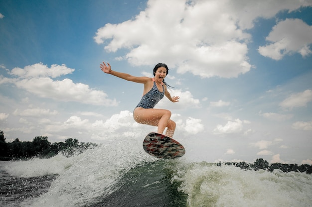 Joven gritando saltando en el tablero de wakesurf en el río