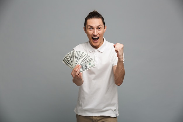 Joven gritando sorprendido sosteniendo dinero hace gesto de ganador.