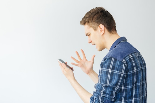 Joven gritando en el teléfono. Hombre hablando por teléfono sobre un fondo gris claro