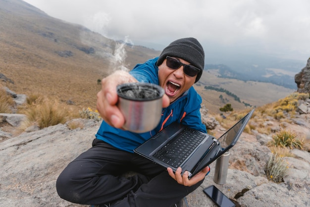 Joven gritando triunfante sosteniendo café feliz en la montaña