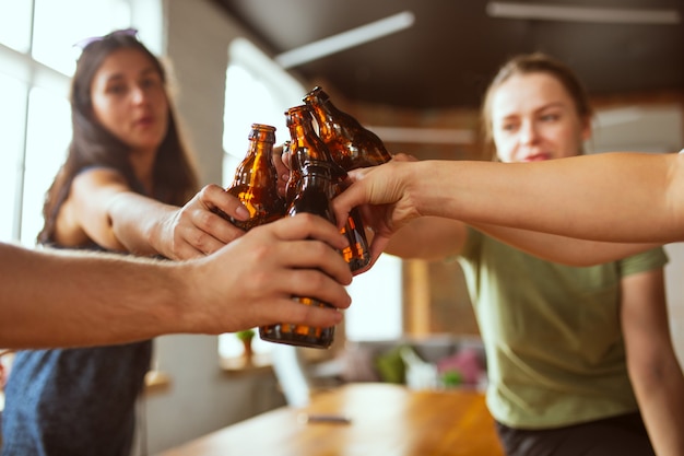 Joven grupo de amigos bebiendo cerveza divirtiéndose riendo y celebrando juntos cerca tintineo