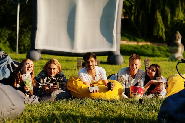 Joven grupo multiétnico de personas viendo películas en poof en cine al aire libre.