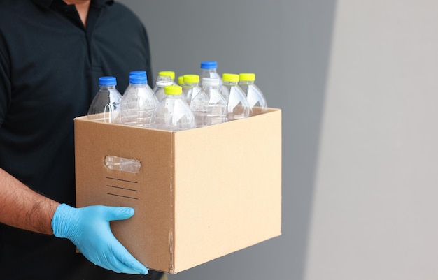 Un joven con guantes de goma dispuso botellas de plástico en una caja de cartón. Él asume que las botellas de plástico se convertirán en basura antes de tirarlas a la basura.
